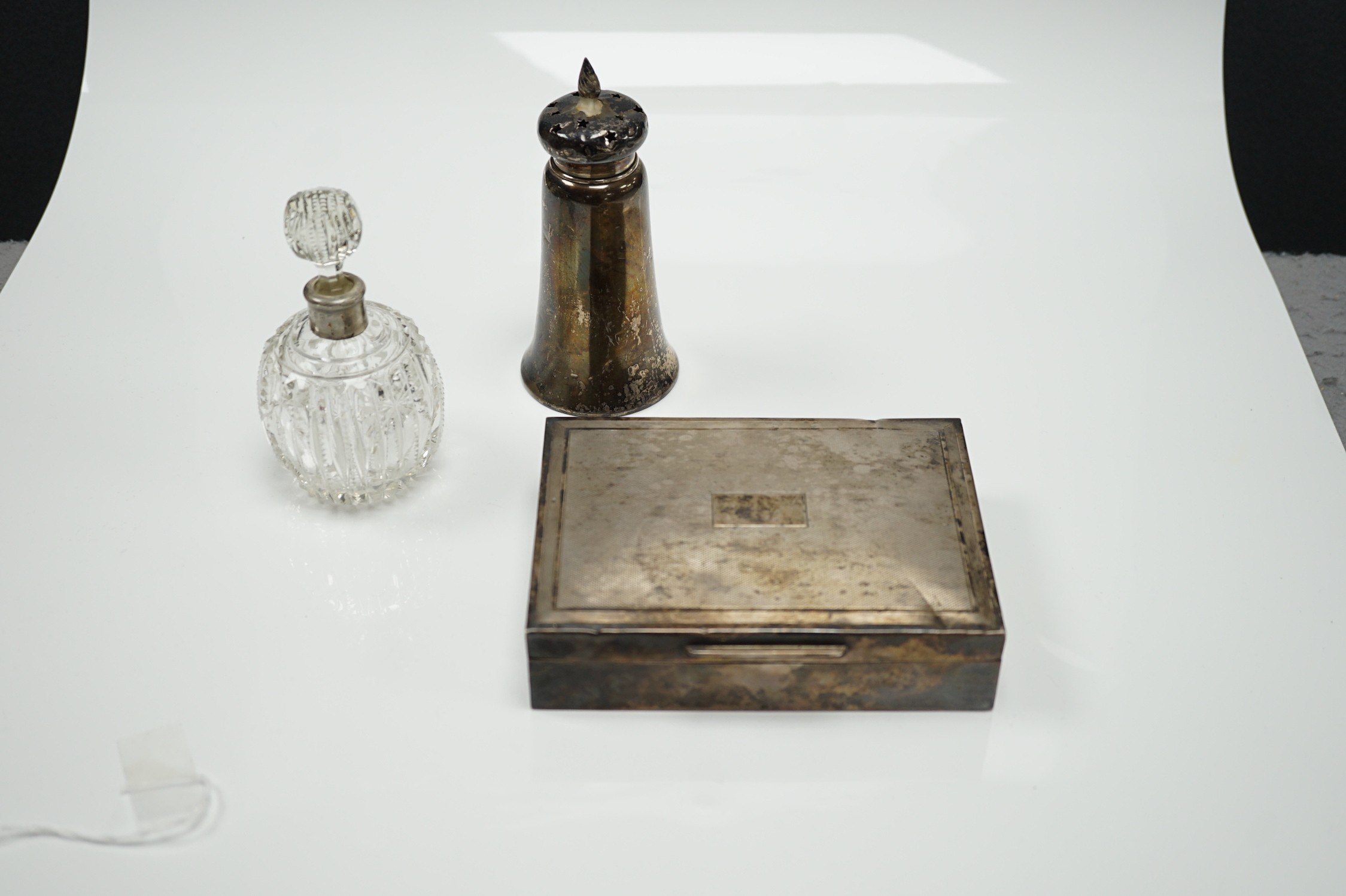 A 1970's engine turned silver mounted rectangular cigarette box, a silver mounted glass sugar caster and a similar scent bottle.